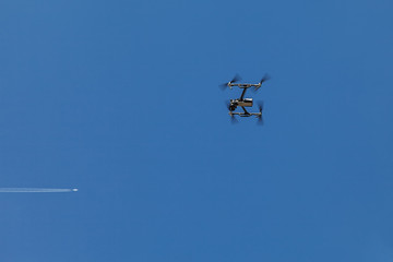 A quadrocopter suspended in the air against a blue sky and a flying plane