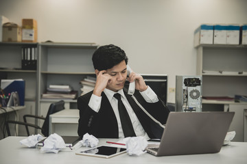 Obraz premium Businessman stress from hard work on the desk at office dark tone.take with boss on telephone,thailand people