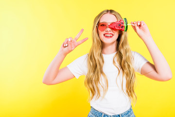 beautiful happy girl in sunglasses with lollipop in shape of watermelon doing Peace Sign On yellow