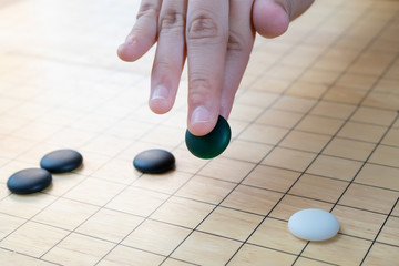 Obraz na płótnie Canvas black stone in hand playing weiqi, igo, baduk game over wooden board - it's an ancient chinese board game