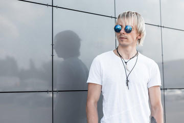 Handsome young hipster blond man in blue round sunglasses with stylish hairstyle in a trendy white...