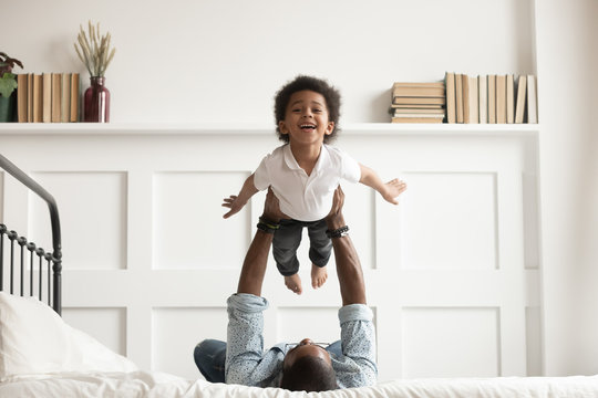 Happy african kid boy flying in fathers arms on bed