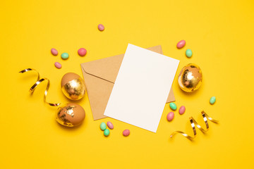 Blank sheet of paper and an envelope with golden eggs of multicolored confetti on a bright yellow background.