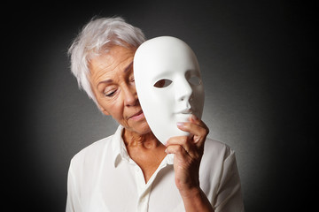 older woman with white hair hiding sad face behind mask - depression or personality concept