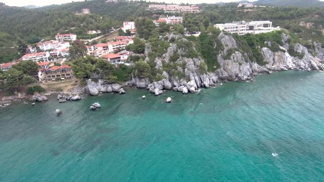 Aerial view of turquoise sea coast with rocks below the tourist village and hot springs facilities in the area of Agia Paraskevi in Halkidiki Greece, sideways movement by drone