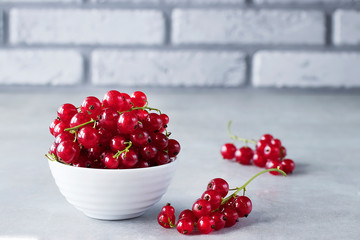 Fresh red currants in a white bowl on a gray background.