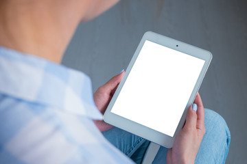 Over shoulder closeup view: woman hands holding digital tablet computer device with white blank screen in home interior. Mock up, copyspace, template, entertainment and technology concept