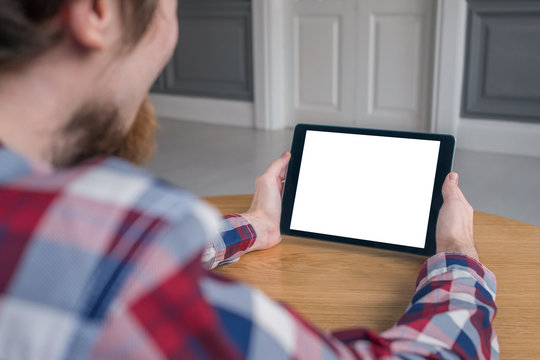 Mockup image: over shoulder close up view of man looking at modern digital tablet computer device with white blank screen. Mock up, copyspace, leisure time, template and technology concept