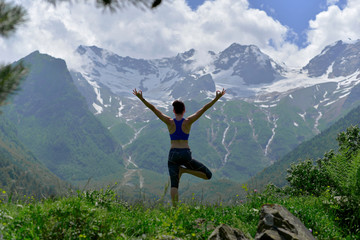 Young sports woman doing yoga on the green grass in the summer on the background of snowy mountains.