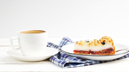 Cup of coffee and piece of cake with cottage cheese souffle and plum decorated with almonds and blueberries on white wooden table