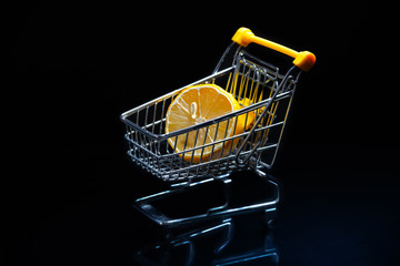 Close-up of shopping carts on black background.Trolley, Sale concept. Isolated over black background in a cart lies a lemon.