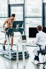 doctor sitting at computer desk and conducting endurance test with sportsman in gym