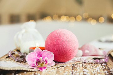 Pink bath ball with orchid flower, scented candle and bath salt on wooden tray in bath room. Therapy concept. Taking a relaxing bath.