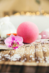 Pink bath ball with orchid flower, scented candle and bath salt on wooden tray in bath room. Therapy concept. Taking a relaxing bath.