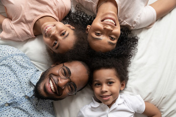 Happy african family looking at camera on bed, top view - Powered by Adobe