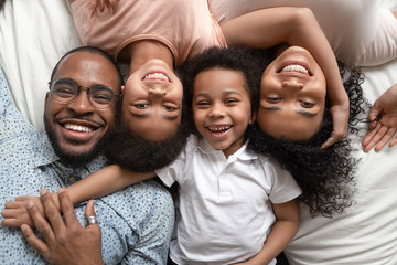 Happy african family lying on bed cuddling, portrait, top view