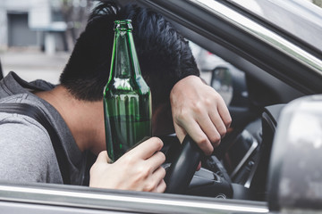 Young asian man drives a car with drunk a bottle of beer and fall asleep behind the wheel of a car - obrazy, fototapety, plakaty