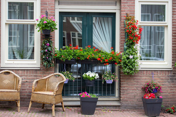 Fototapeta na wymiar Calm terrace with chairs and flower pots. Exterior of unknown brick building in Amsterdam, Netherlands. Entrance with windows and flowers. Facade decoration in Europe. 