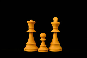 White King, Queen and Pawn as one child family concept. Three standard chess wooden pieces on black background