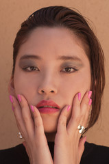 Portrait of Asian Model posing with both hands on her face and pink nail varnish