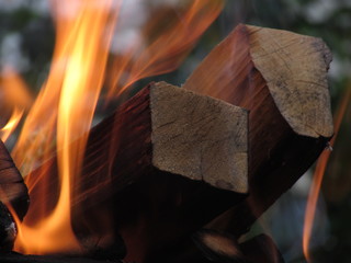 A burning orange bright flame of fire engulfed sections of birch blackened, smoked square logs