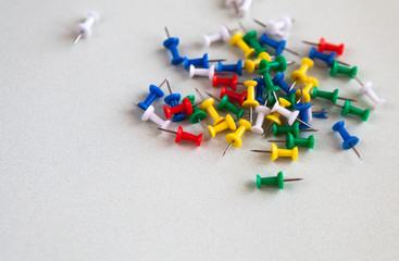 Multi-colored pushpins or thumbtacks scattered around a white wooden surface. One pin sticks up - Powered by Adobe