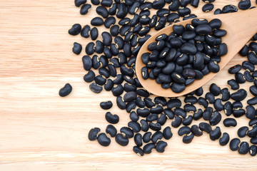 Close-up Raw black beans in a wooden spoon on wooden background, top view.