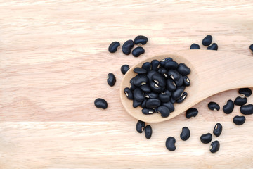 Close-up Raw black beans in a wooden spoon on wooden background, top view.