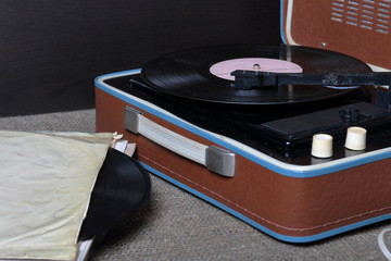 An old gramophone with a vinyl record mounted on it. Next to shabby paper envelopes are other...