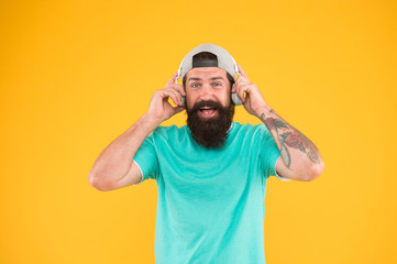 Fototapeta na wymiar There is music for every man. Bearded man in trendy hipster style smiling on yellow background. Happy man with beard and mustache wearing modern headphones. Brutal man enjoy listening to music