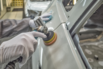 Employee in the shop painting the car body polishes painted body parts