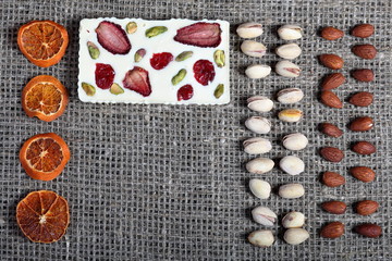 Dried orange slices, pistachios and almonds are lined up in rough linen fabric. White chocolate decorated with dried fruit.
