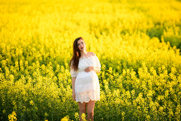 Naklejka na ściany i meble Pregnant girl on the rapeseed field. cute young woman waiting a baby