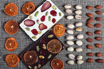 Dried orange slices, pistachios and almonds are lined up in rough linen fabric. Dark and white chocolate decorated with dried fruit.