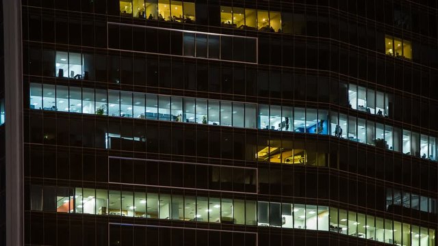 Close up view to office windows of skyscraper in downtown at evening, working people within. Dubai, United Arab Emirates