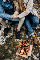 Top view on the fire burning on the frozen ground in the forest and Caucasian man and woman sitting by and holding hands. View from above.