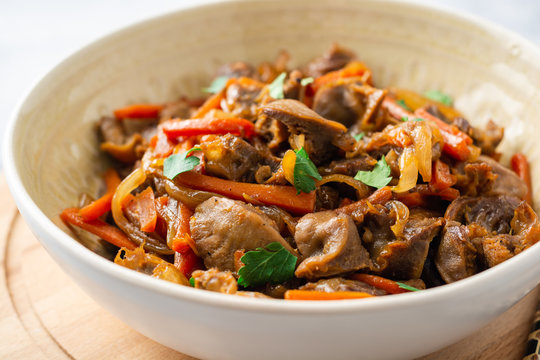 Fried chicken gizzards with carrot and onion in bowl on concrete background. Selective focus.