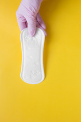 a pink-gloved hand holds a daily thin menstruation pad during the menstrual period of a woman on critical days, gynecological menstrual cycle on yellow background with copy space