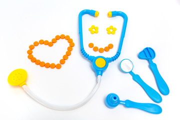 Blue stethoscope, otoscope, hammer, dental mirror Isolated on white background. Medicine concept. Children's toys by profession doctor. A heart is by orange pills. Stethoscope smiles.