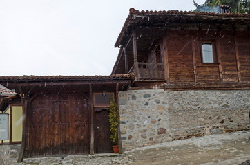 Fototapeta na wymiar Authentic unique residential district with painted in bright colors houses, stone walls, wooden windows, verandahs and picturesque eaves in snowfall, Koprivshtitsa town, Bulgaria, Europe 