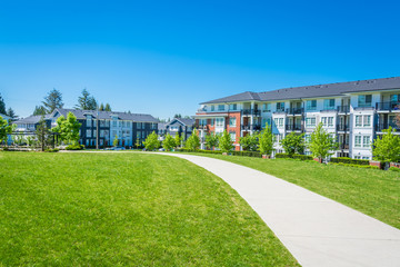 Concrete pathway across huge green lawn in front of residential condo building. Apartment building on sunny day with blue sky.