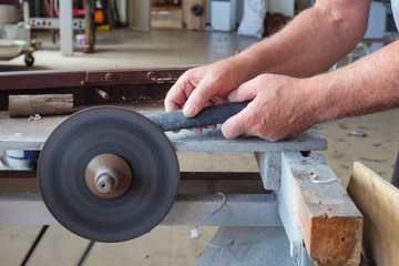 Hands of worker wich is sharpering knife on grindstone