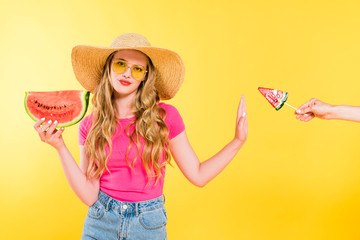 dissatisfied girl with watermelon gesturing and refusing lollipop on yellow