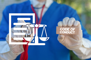 Medical worker holding wooden block with code of conduct collocation and touching document sheet with scales icon. Code of conduct health care concept.