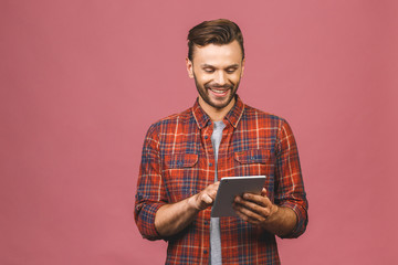 Happy casual man using tablet computer isolated on a pink background.