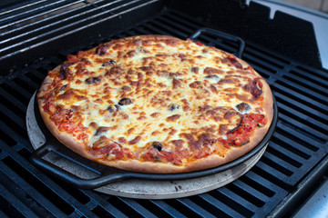 Pepperoni, cheese and tomato pizza being made on a cast iron skillet and on a barbeque grill outoors