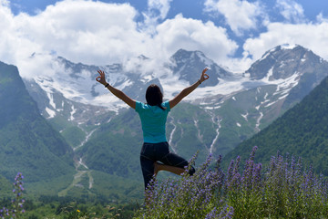 Young sports woman doing yoga on the green grass in the summer on the background of snowy mountains.