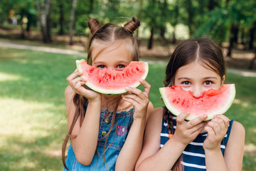Two cute little girls eating watermelon in park in summertime
