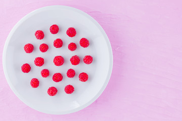 Raspberries on a white plate. Red raspberry berries on a pink background. Berries for vegan. Summer concept. Minimalist food. Top view. Copy space