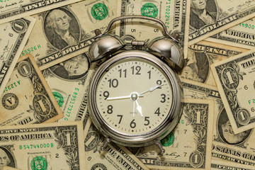 Alarm clock on carpet of dollar bills, time is money.
